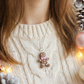 Person wearing a beige sweater with a gingerbread man ornament, surrounded by Christmas decorations.