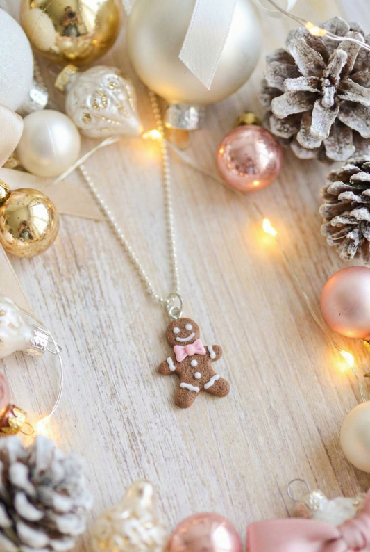 Necklace with a gingerbread man pendant surrounded by Christmas ornaments on a wooden surface.