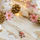 Decorative Christmas scene with small trees, pinecones, flowers, and a gingerbread man necklace on a wooden surface.