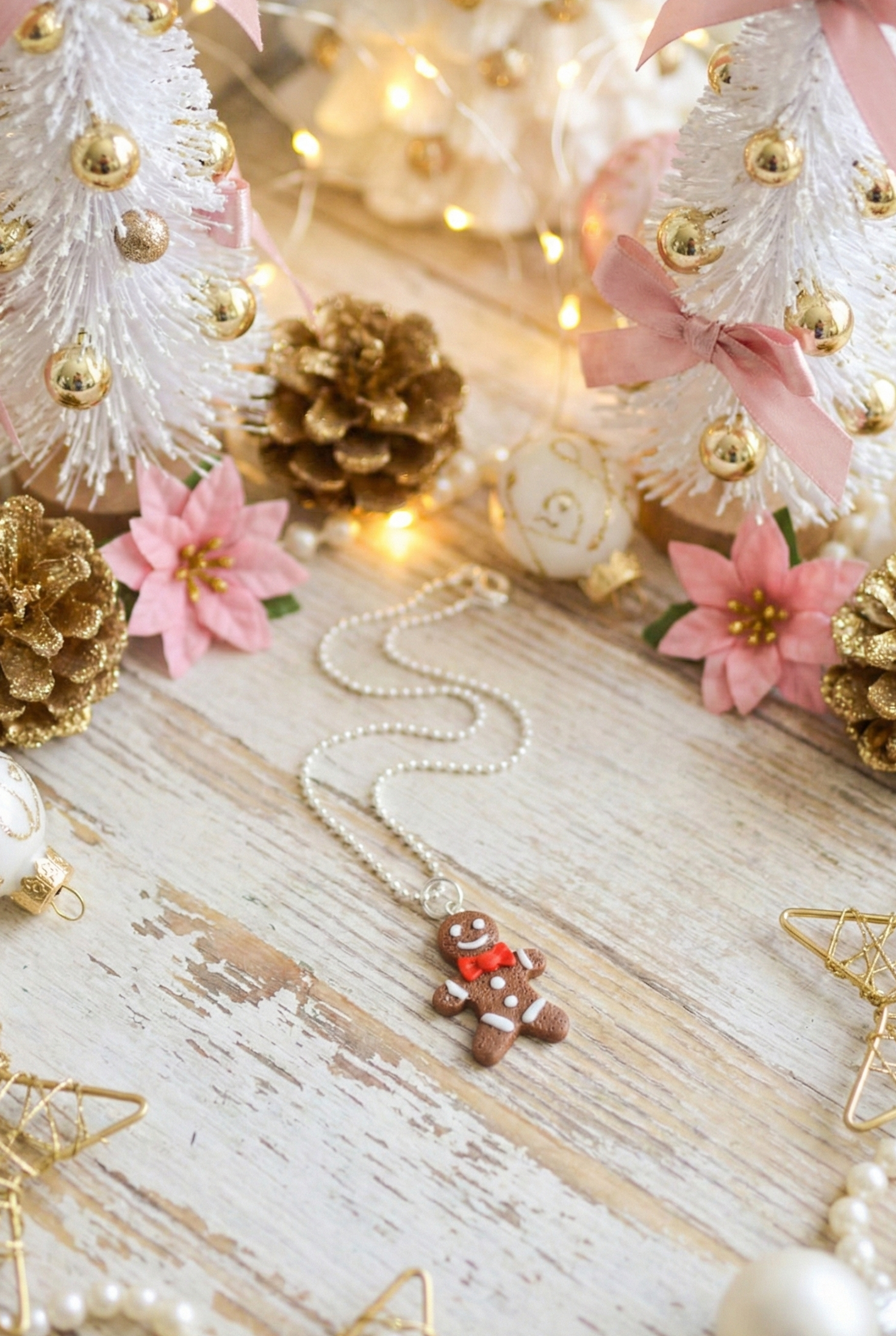 Decorative Christmas scene with small trees, pinecones, flowers, and a gingerbread man necklace on a wooden surface.