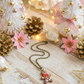 Decorative Christmas scene with small trees, pinecones, flowers, and a necklace on a wooden surface.