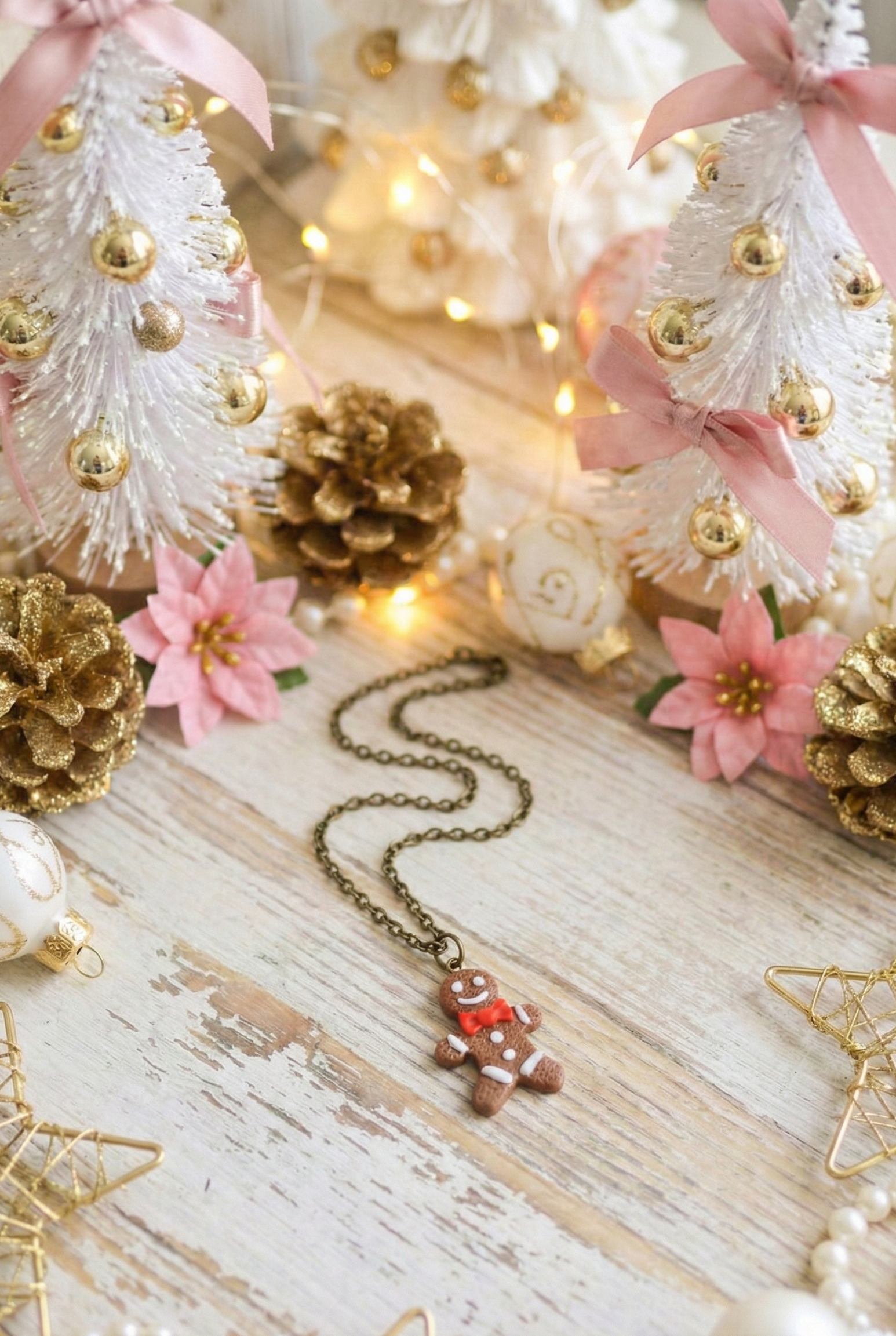 Decorative Christmas scene with small trees, pinecones, flowers, and a necklace on a wooden surface.