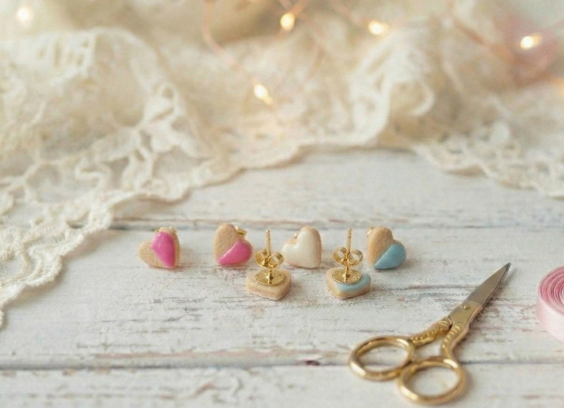 Set of small heart-shaped cookie earrings on a wooden surface with lace and scissors in the background.
