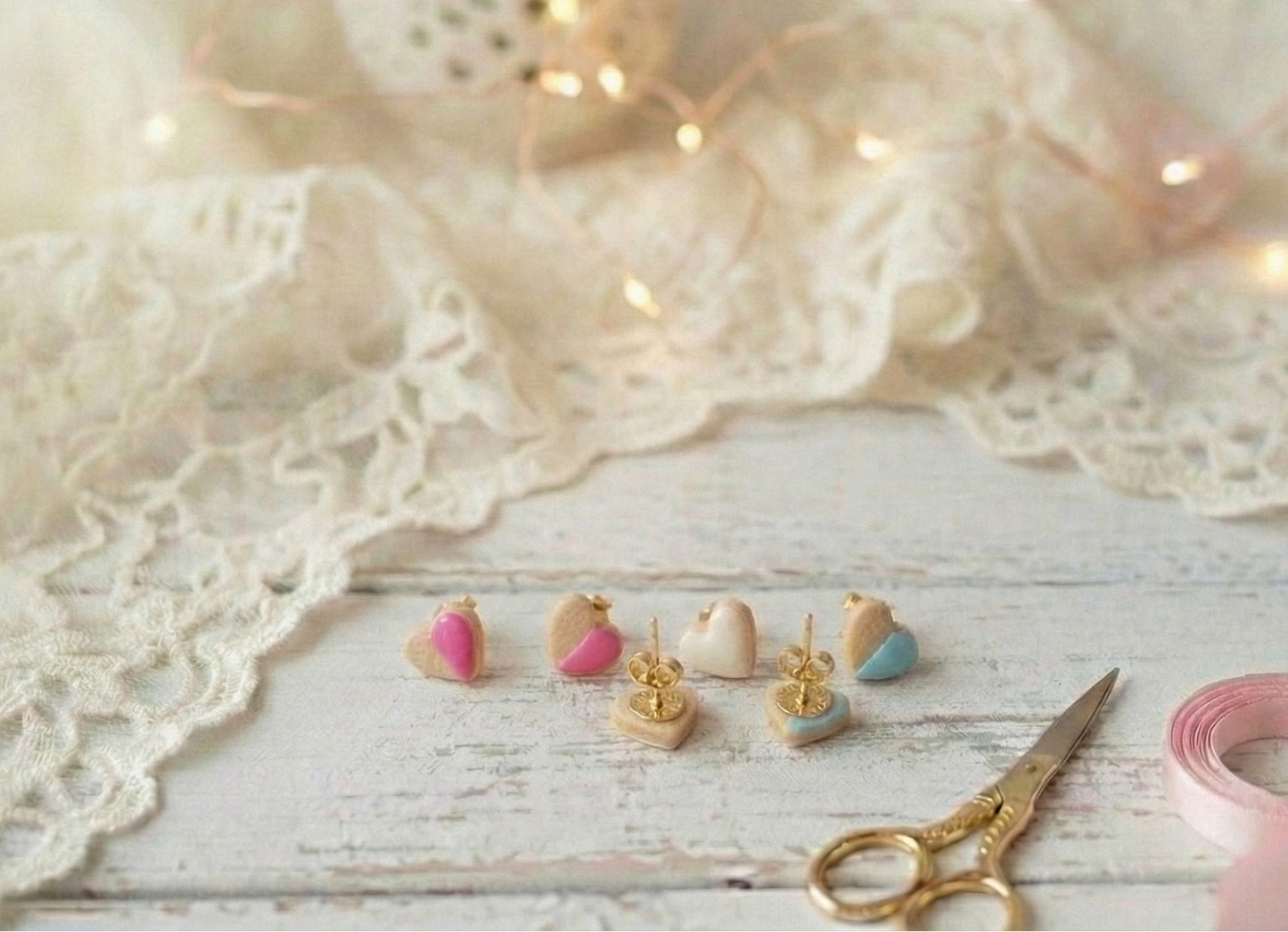 Set of small earrings on a wooden surface with lace fabric and decorative lights in the background.