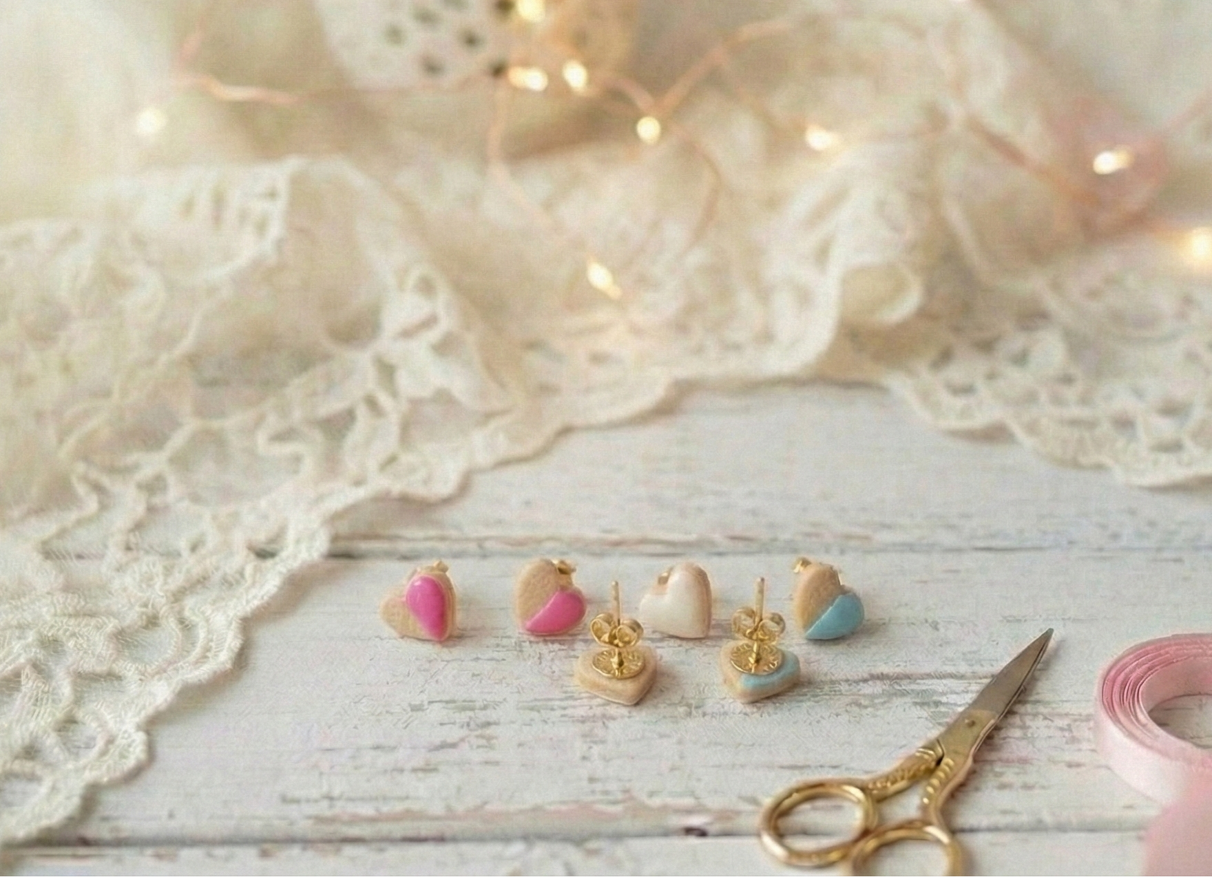Set of small earrings on a wooden surface with lace fabric and decorative lights in the background.