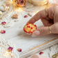 Hand holding a small cherry pie miniature with red berries on a decorative table setting with teacups and spoons.