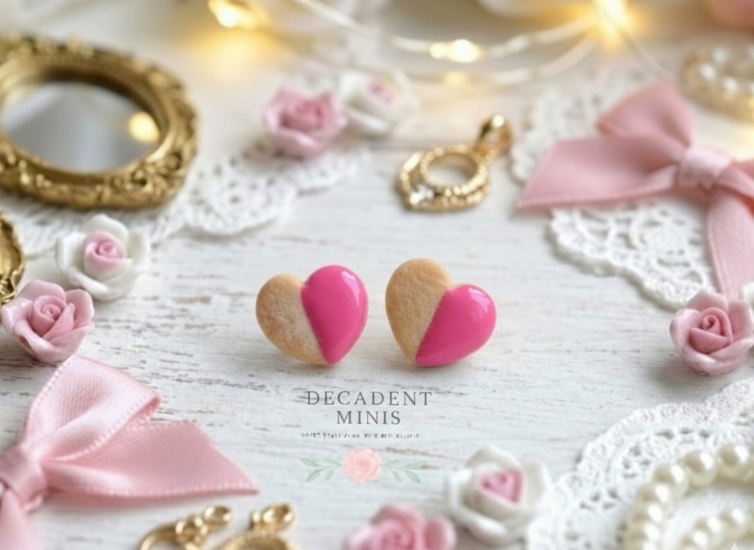 Heart-shaped cookie earrings with pink and gold design on a decorative background with flowers and ribbons.
