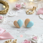 Heart-shaped cookie earrings with pastel colors on a decorative background with bows and roses.