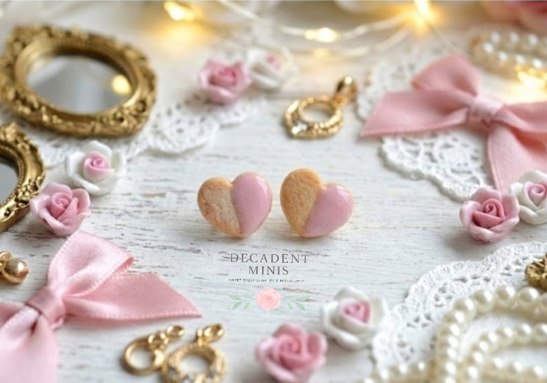 Heart-shaped pink and gold earrings on a decorative background with bows and lace.