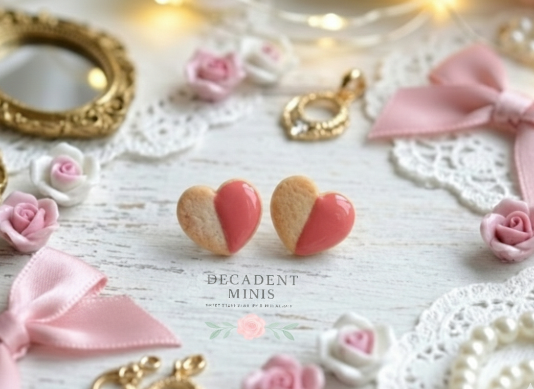 Heart-shaped cookie earrings with strawberry frosting  on a decorative surface with pink roses and gold frames.