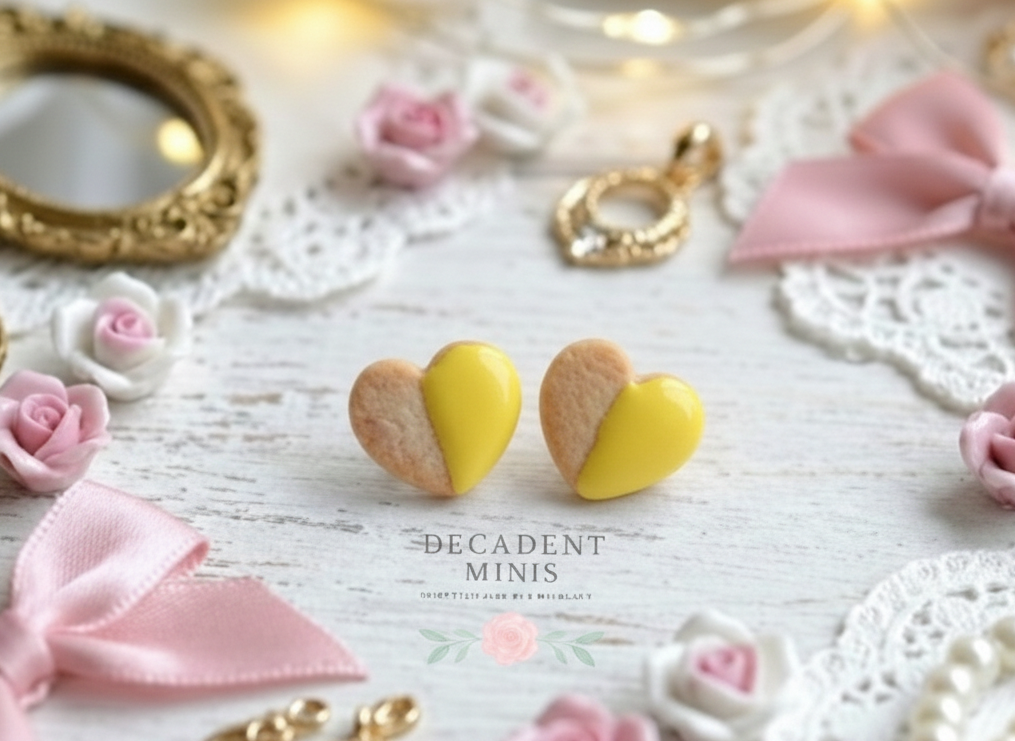 Heart-shaped yellow dipped cookie earrings on a decorative surface with pink bows and flowers.