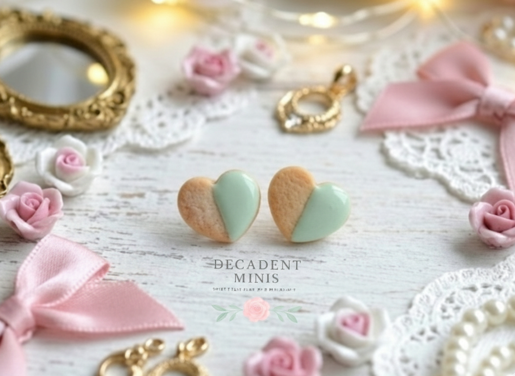 Heart-shaped cookie earrings on a decorative surface with pink bows and gold frames.